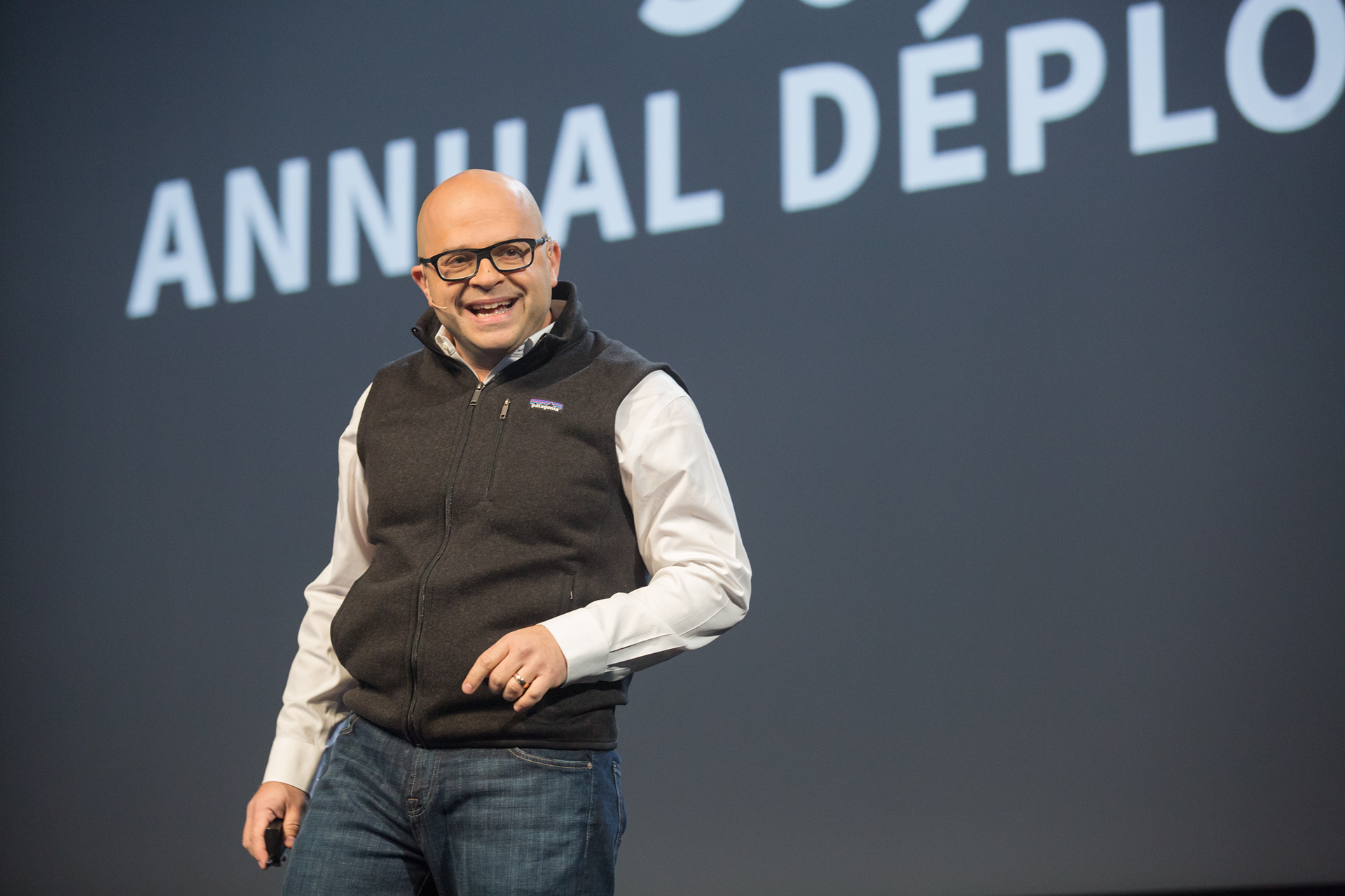 Speaker presenting on stage at annual developer conference with projected text backdrop